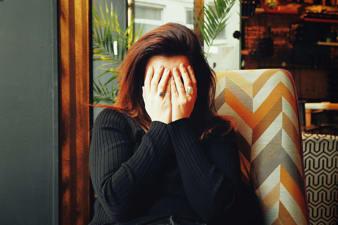 Woman holding her head in her hands, experiencing a chronic headache while sitting on a patterned chair.