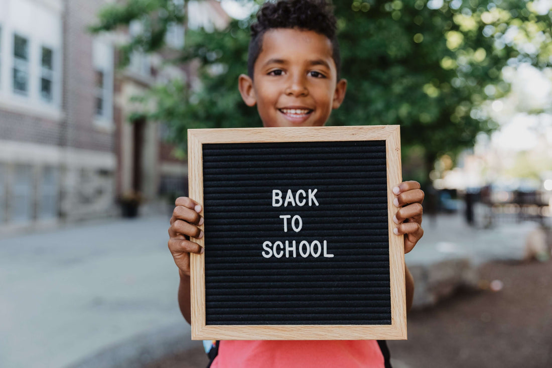 Small boy holding a sign that says, back to school while wearing a back pack.