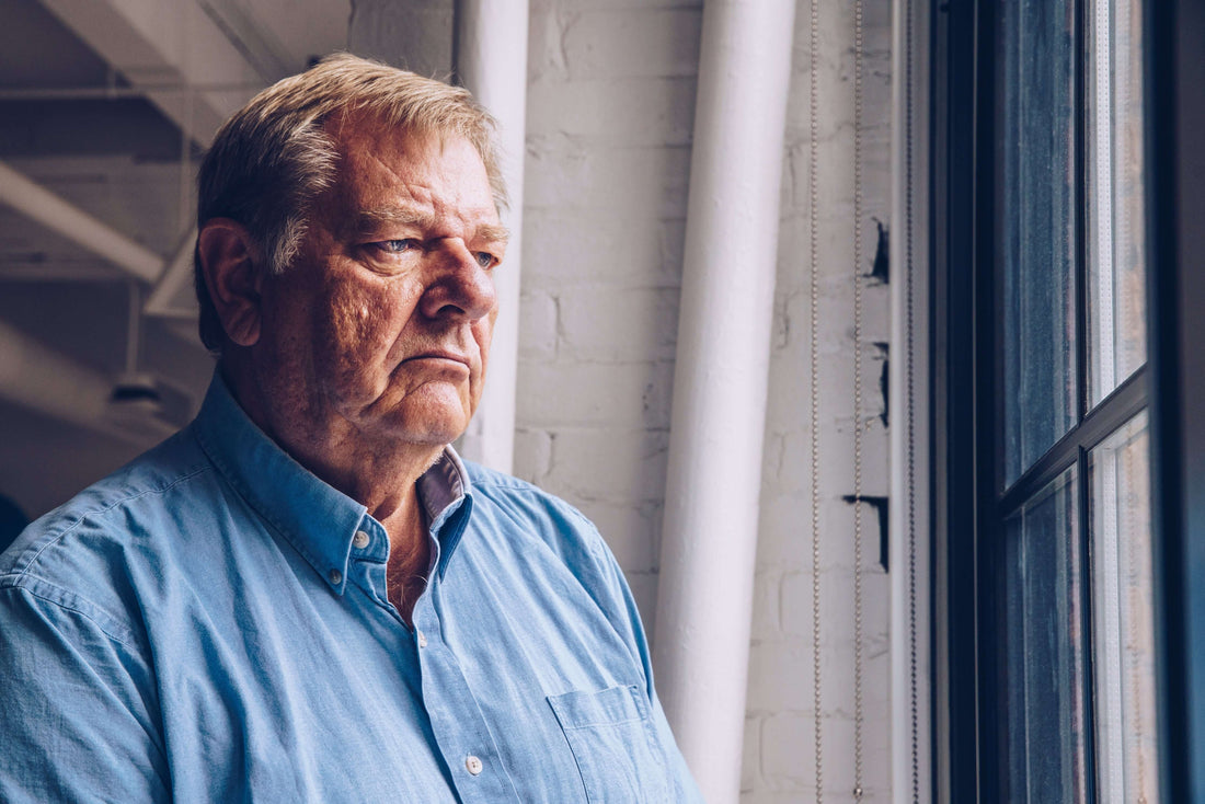 Older man looking out a window, reflecting on his life and past decisions.