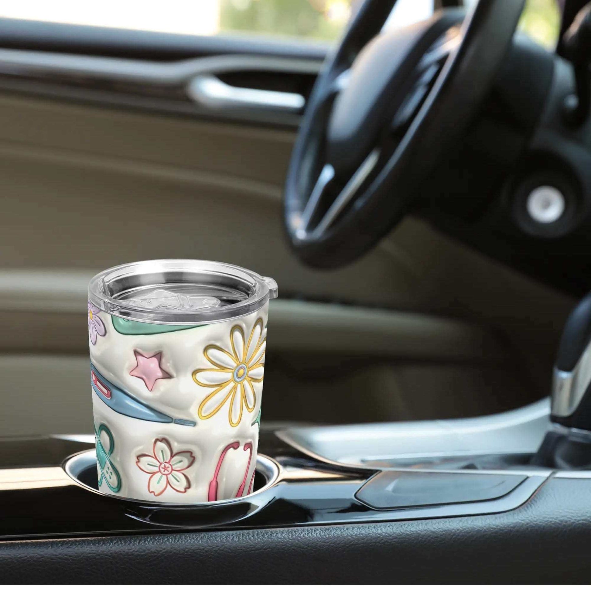 A 20oz 3D Inflated Tumbler - Perfect for Hot & Cold Drinks On-the-Go, featuring a colorful floral design, sits in the cup holder of a car. The double-walled stainless steel construction ensures drinks stay at the perfect temperature, and the splash-proof lid prevents spills. The car's interior showcases a sleek black and beige design, with both the gear shift and part of the steering wheel visible.