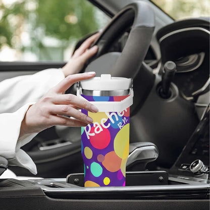 A hand reaching for a colorful, 30oz Nurse Tumbler with Stylish Circle Design and the name "Rachael" personalized on it, sits snugly in a car's cup holder. The car's steering wheel and dashboard are visible, with a blurred greenery background outside the window.