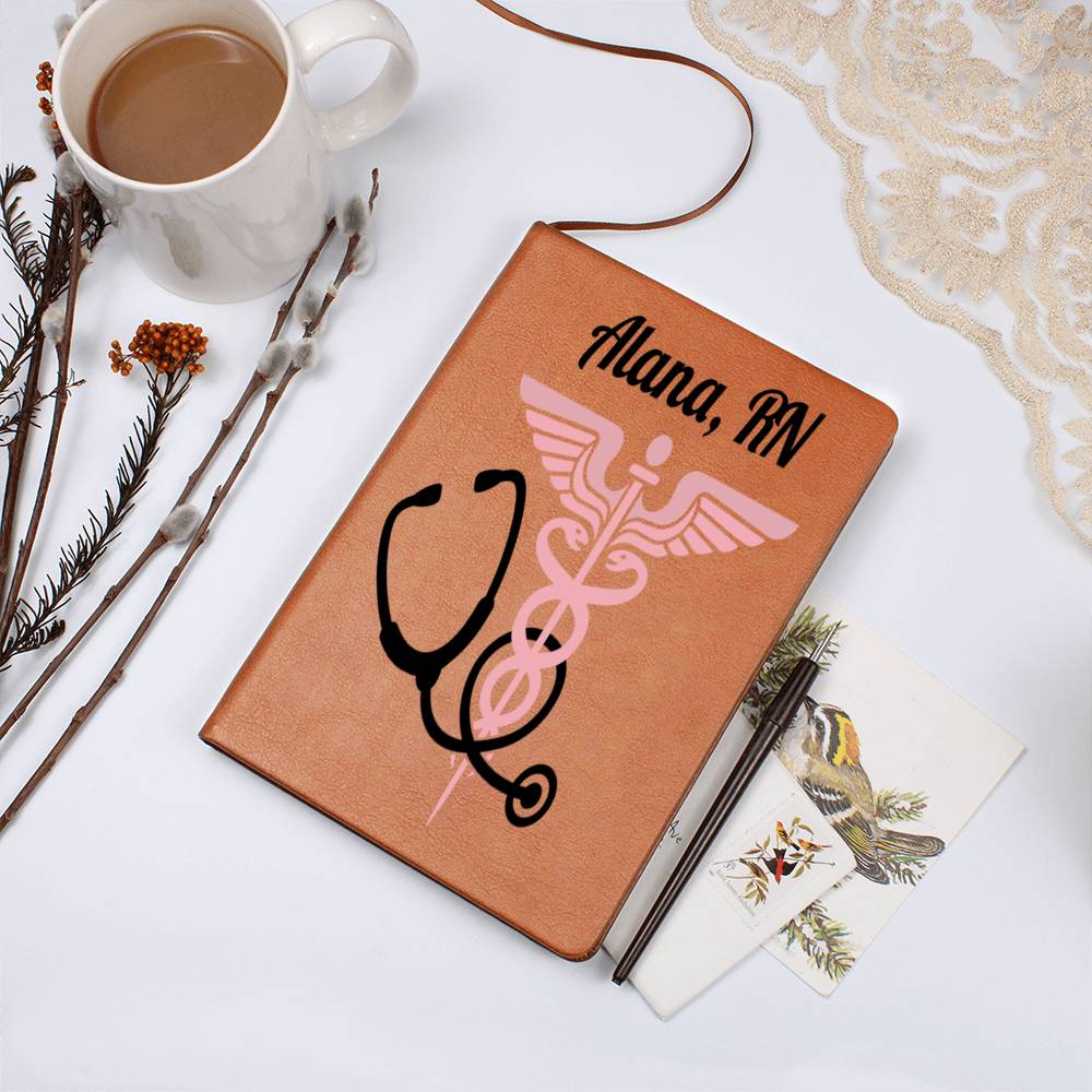 A Custom Medical Journal: Personalized Notebook for Doctors & Nurses - Leather with "Alana, RN" printed on the cover alongside a caduceus and stethoscope. This unique gift is set on a white surface, surrounded by a cup of coffee, a sprig of flowers, a lace cloth, and bird-themed greeting cards.